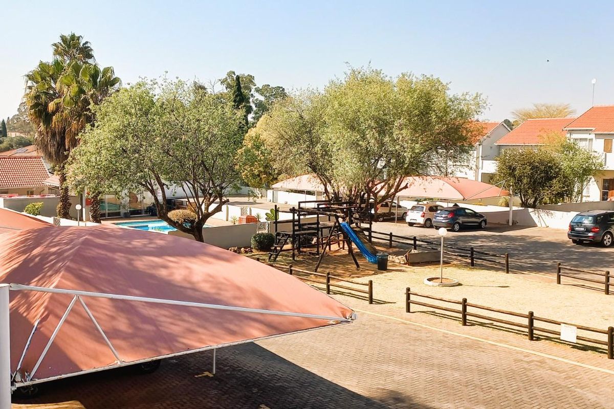 An elevated view of the townhouse complex grounds, featuring paved parking areas with shade cloth carports, a children's play area, and a swimming pool.