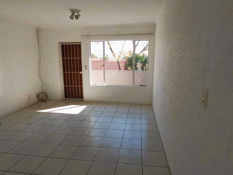 An empty, open-plan living area featuring tiled flooring, a security gate, and a large window providing natural light.