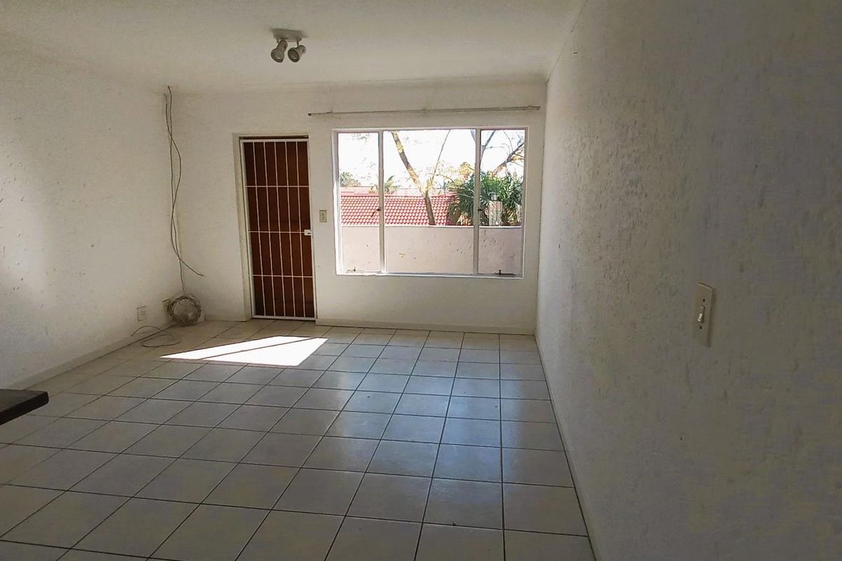 An empty, open-plan living area featuring tiled flooring, a security gate, and a large window providing natural light.