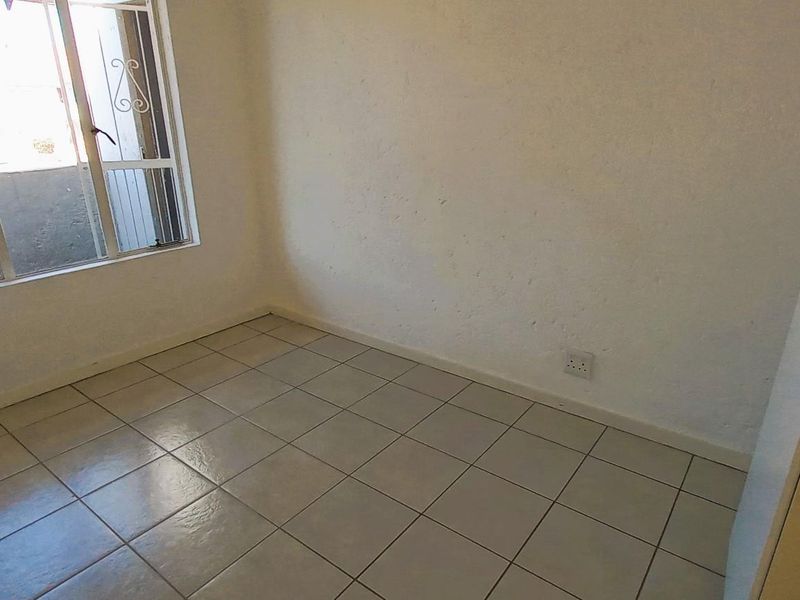 An empty bedroom featuring tiled flooring, a security gate on the window, and neutral wall finishes, ready for personalization.