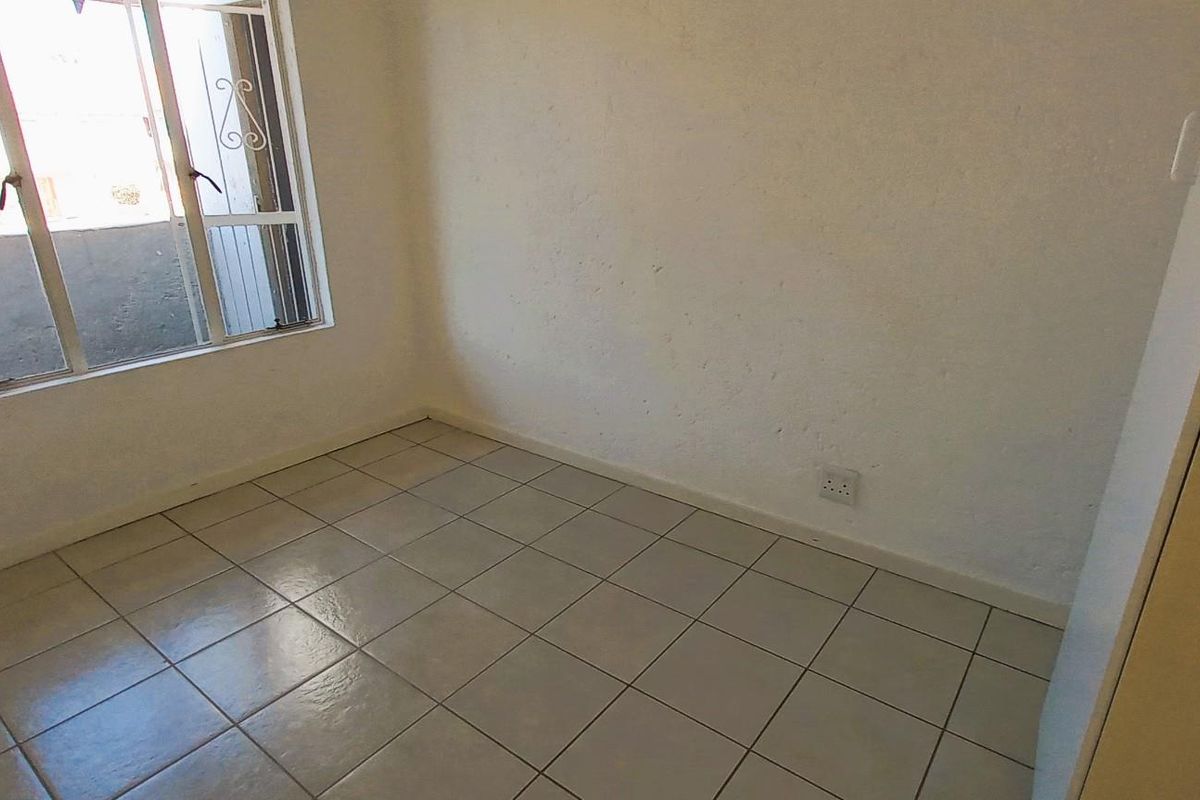 An empty bedroom featuring tiled flooring, a security gate on the window, and neutral wall finishes, ready for personalization.