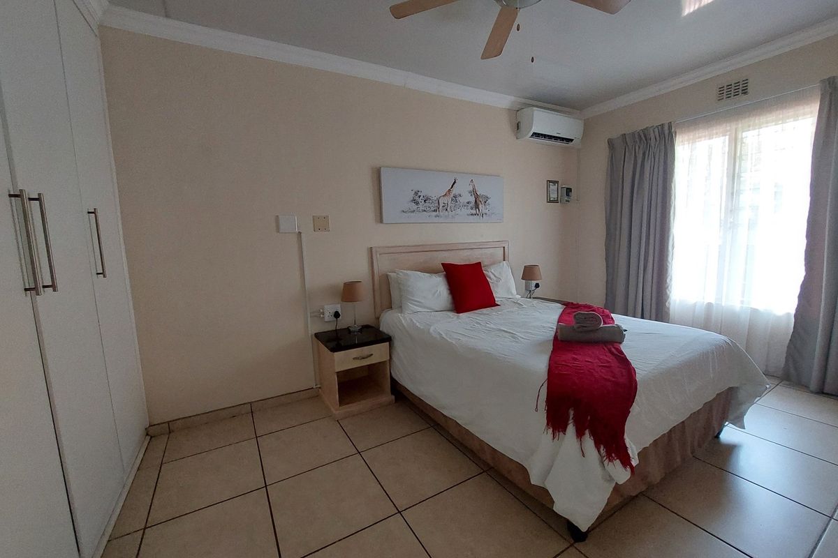 A well-maintained bedroom featuring built-in cupboards, tiled flooring, a ceiling fan, and a wall-mounted air conditioning unit.