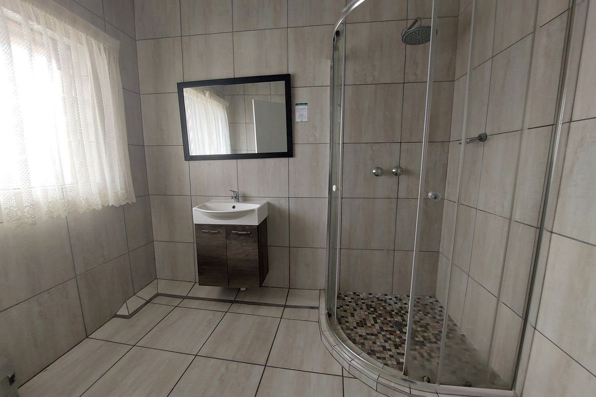 A modern bathroom featuring a corner glass shower enclosure, a wall-mounted vanity with a basin, and neutral floor-to-ceiling tiling.