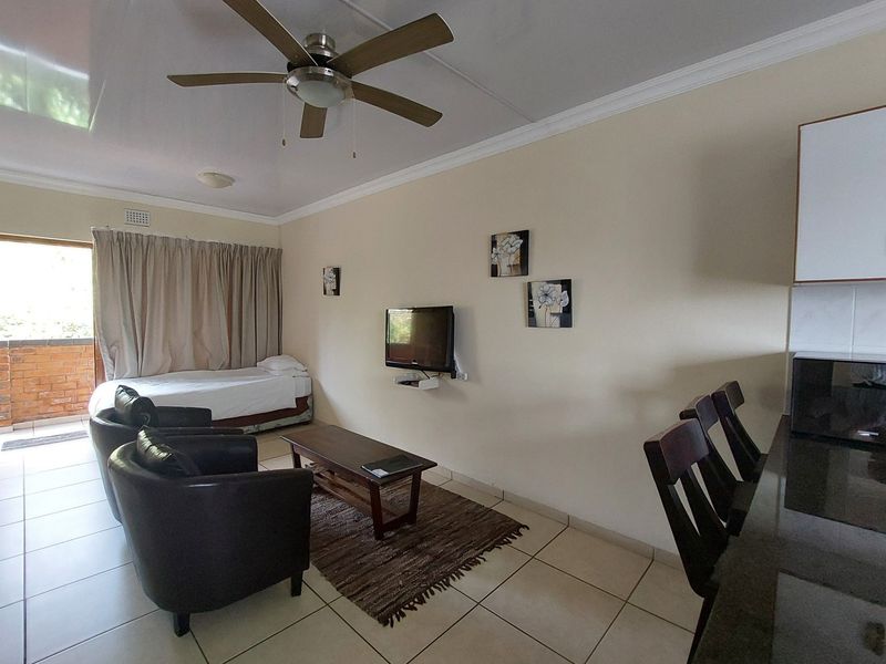 Open-plan living area featuring tiled floors, a ceiling fan, and a breakfast counter, with direct access to an outdoor balcony.