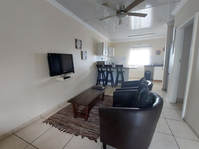 Open-plan living area featuring tiled flooring, a ceiling fan, and a functional kitchen with built-in cabinetry and a breakfast bar.