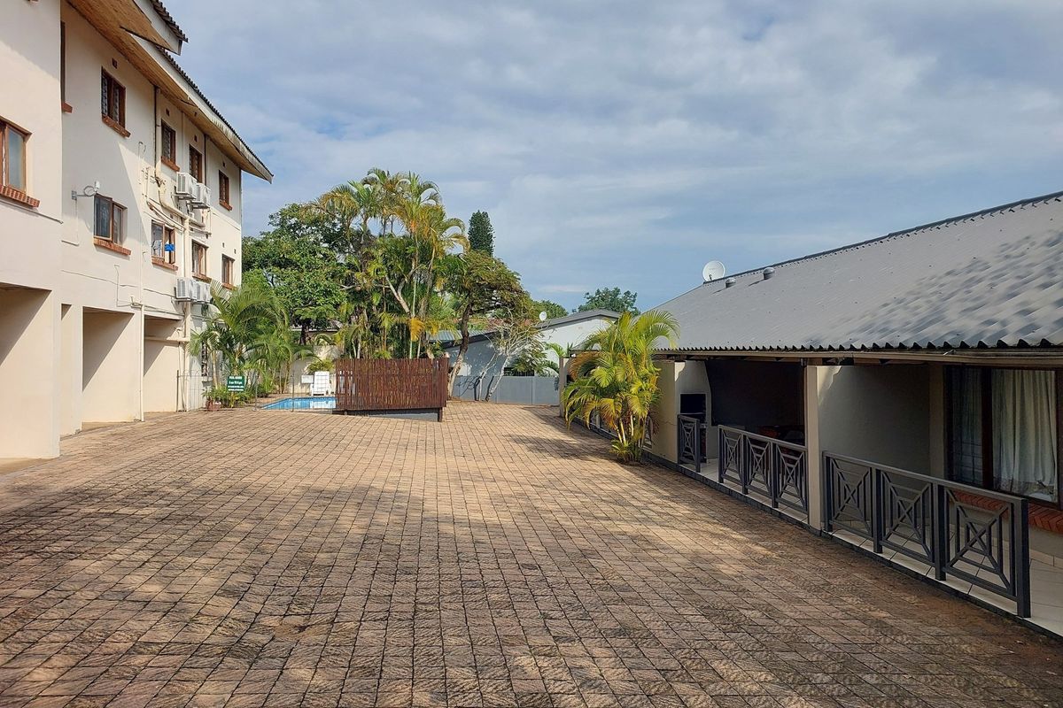 A spacious paved courtyard area between apartment buildings, featuring metal railings, external air conditioning units, and access to a communal swimming pool.