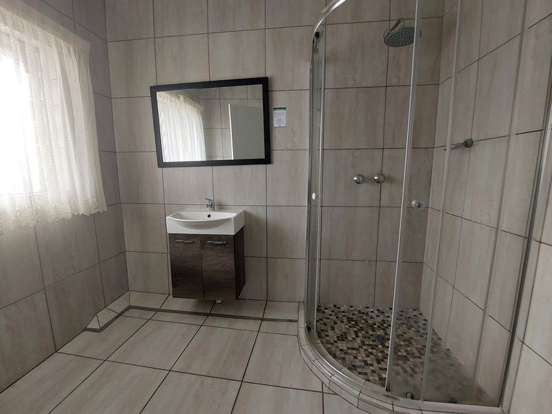 A clean, modern bathroom featuring a corner shower enclosure, wall-mounted vanity with basin, and neutral floor-to-ceiling tiling.