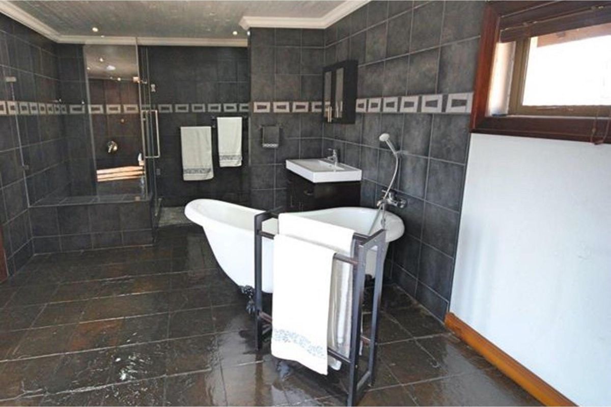 A spacious bathroom featuring dark slate-style wall and floor tiling, a freestanding clawfoot bathtub, a separate glass-enclosed shower, and a modern vanity basin.