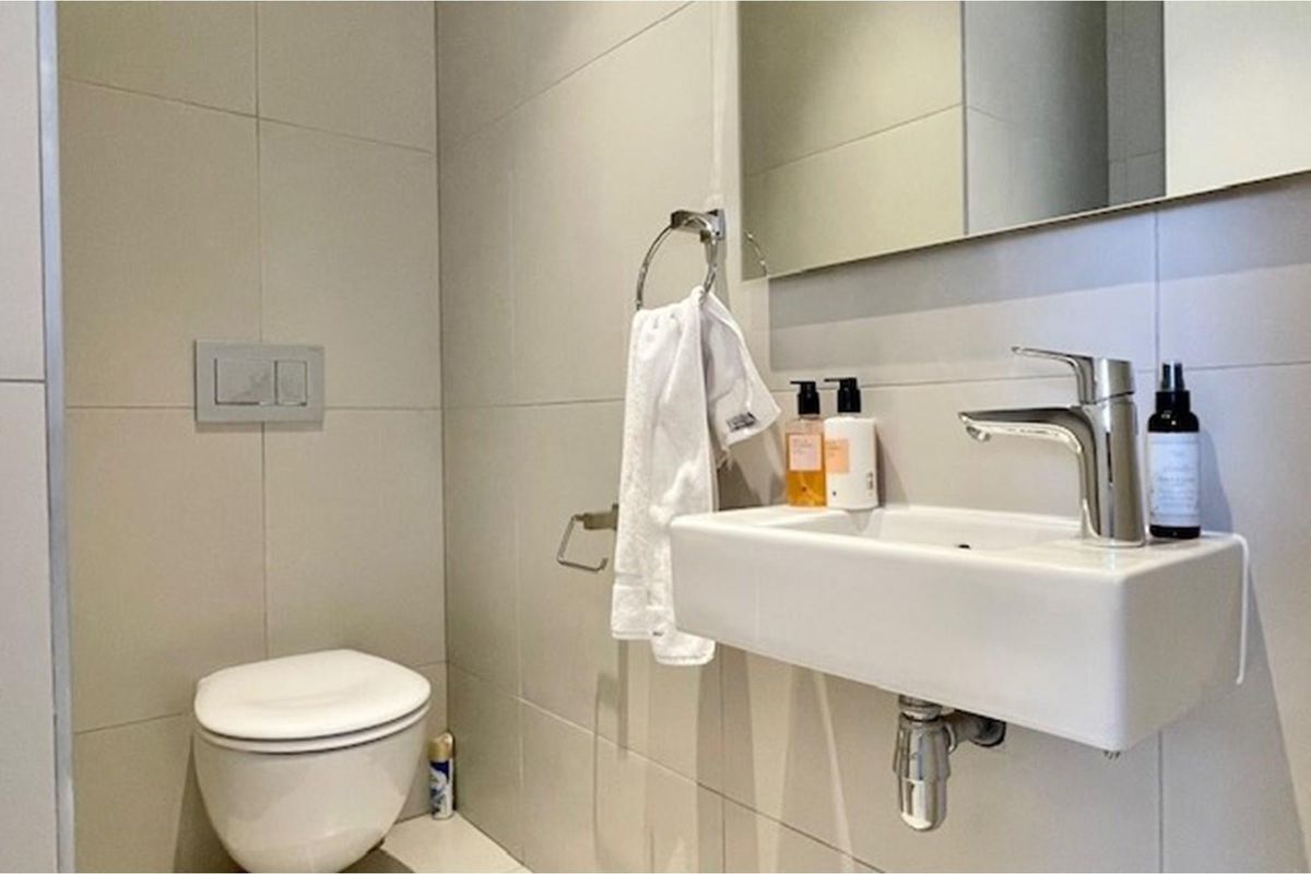 A modern bathroom featuring a wall-mounted basin, chrome faucet, and a concealed cistern toilet with neutral wall tiling.