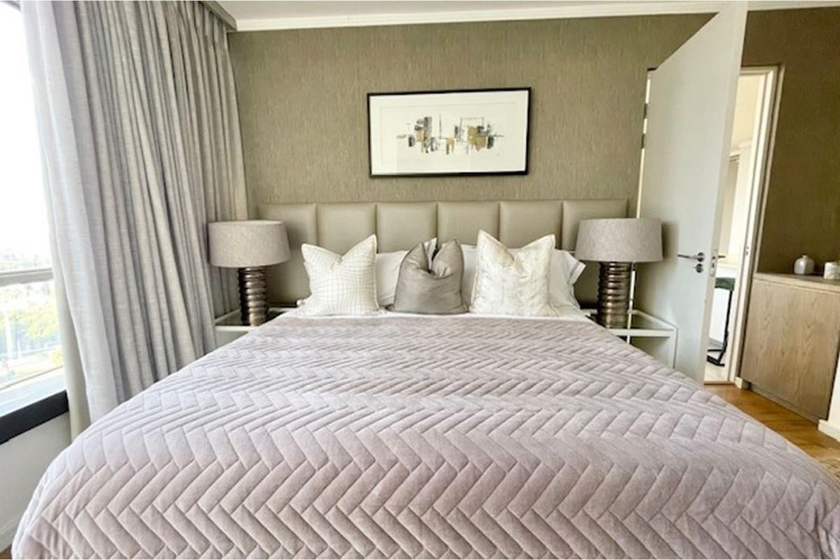 A well-appointed bedroom featuring a neutral color palette, textured accent wall, and floor-to-ceiling curtains providing ample natural light.