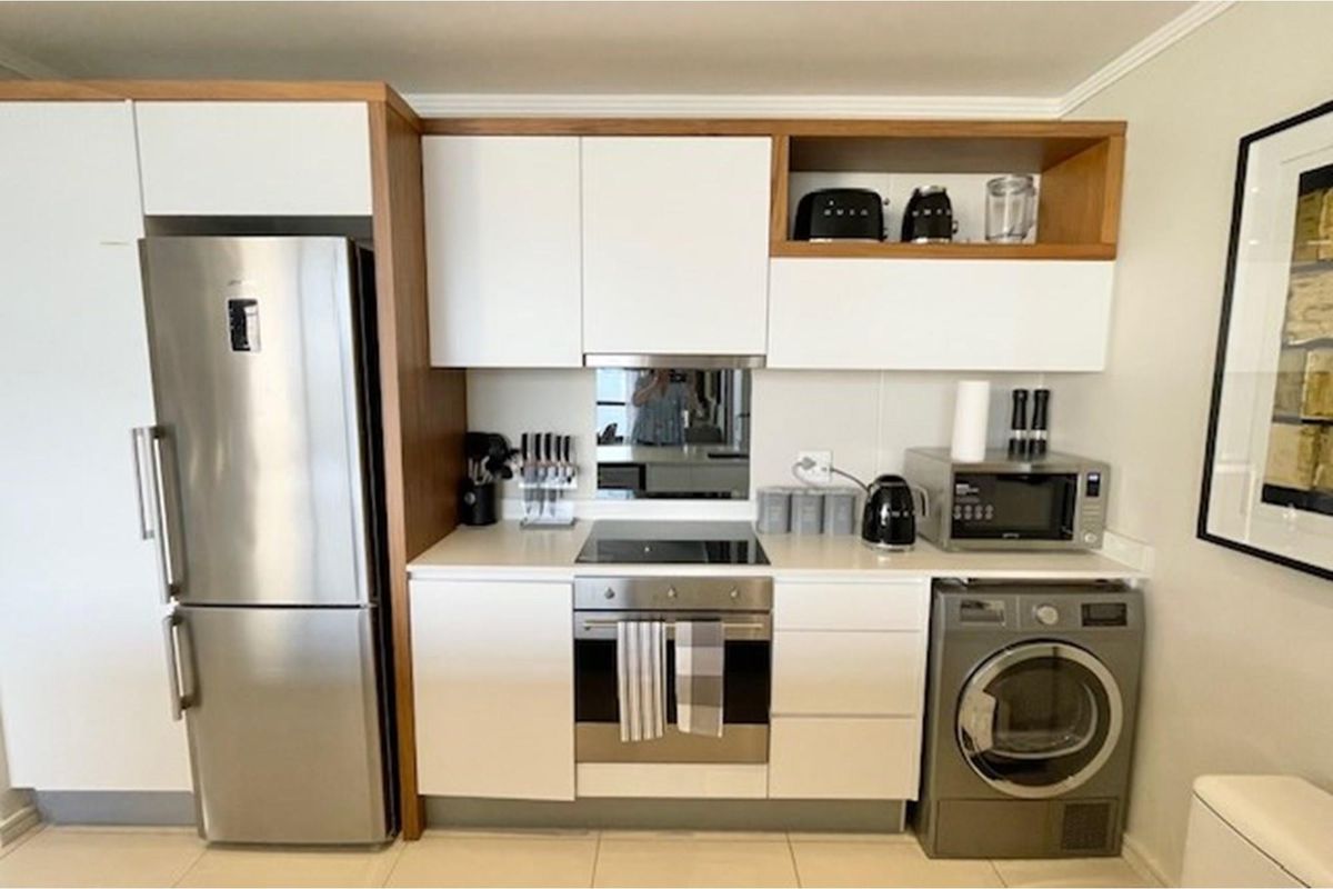 Modern compact kitchen featuring white cabinetry with wood accents, integrated stainless steel oven, hob, and space for a washing machine.