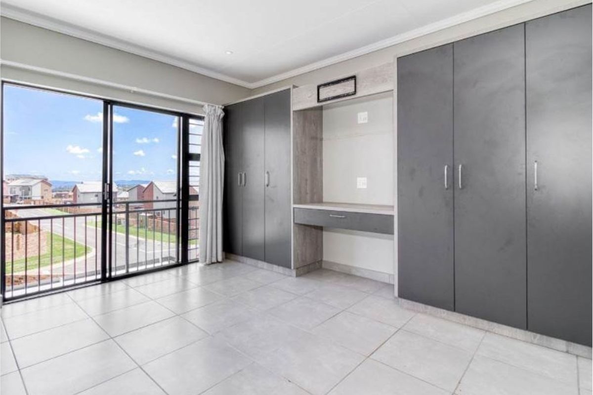A bright bedroom featuring large sliding glass doors, tiled flooring, and extensive built-in cabinetry with an integrated desk area.