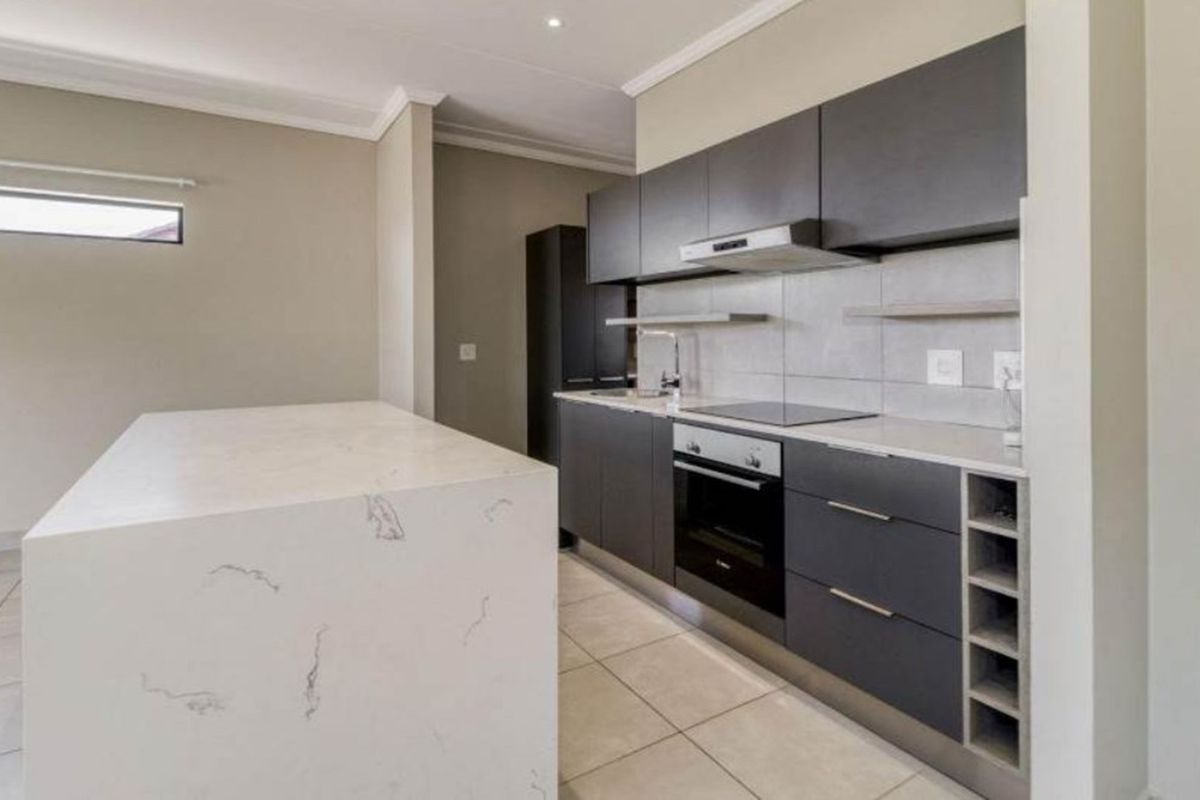 Modern kitchen featuring dark cabinetry, stone-topped island, built-in oven, electric hob, and extractor fan with tiled flooring.