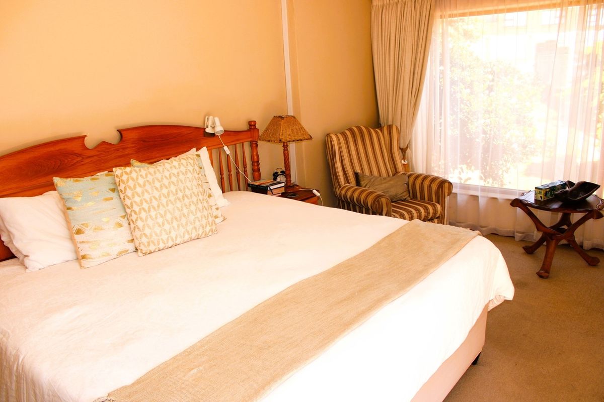 A comfortable bedroom featuring neutral wall tones, carpeted flooring, and large windows with curtains allowing natural light into the space.