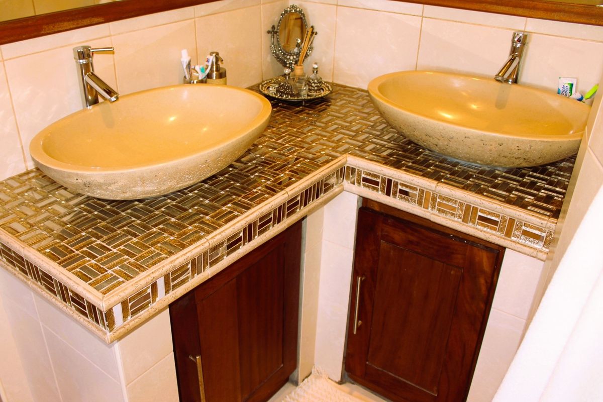 A bathroom vanity featuring dual stone vessel sinks, custom wooden cabinetry, and decorative mosaic tile countertops.