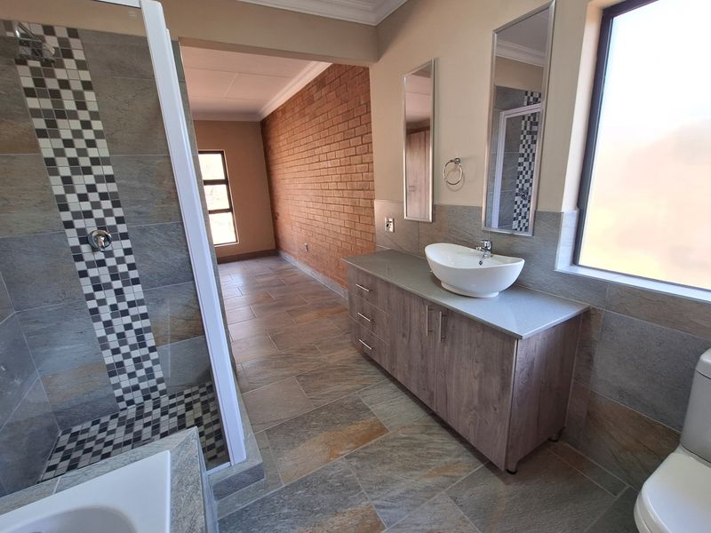 Modern bathroom featuring a walk-in shower with mosaic tile accents, a vessel sink vanity, and tiled flooring, adjacent to a brick-walled living space.