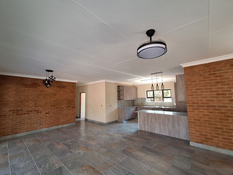 Open plan living and kitchen area featuring exposed brick walls, modern cabinetry, stone-look floor tiles, and contemporary pendant lighting.