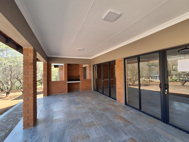 A spacious covered patio featuring exposed brick pillars, built-in braai, and large sliding glass doors providing seamless indoor-outdoor flow.
