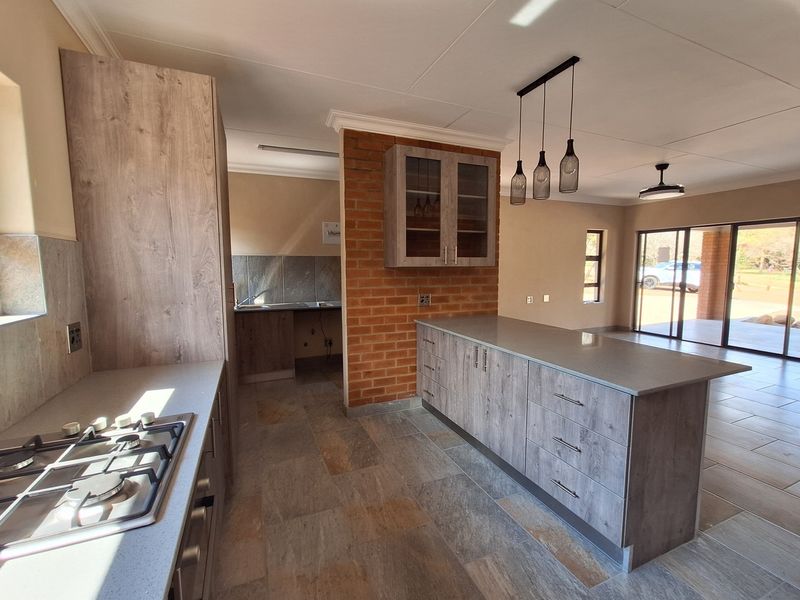 Modern open-plan kitchen featuring a central island, built-in gas hob, stone countertops, and a distinctive exposed brick feature wall.