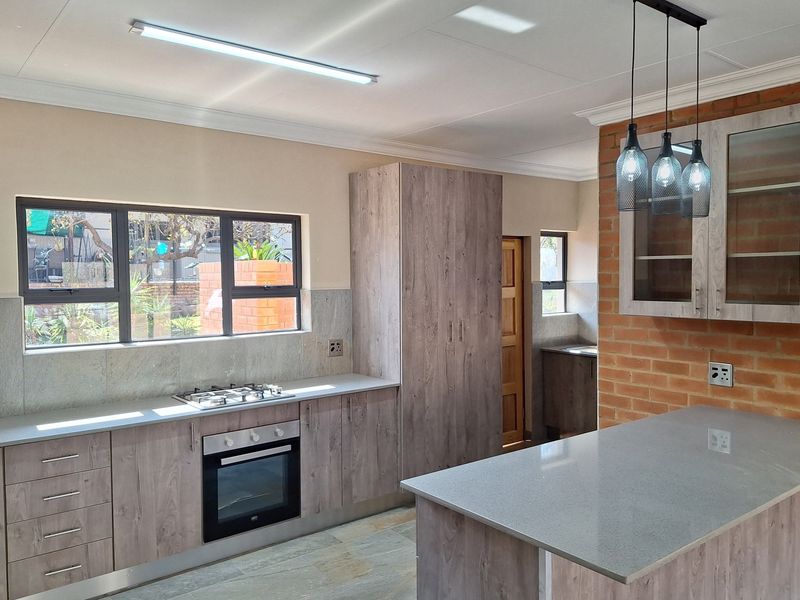 Modern kitchen featuring wood-look cabinetry, stone countertops, a built-in oven and gas hob, and a breakfast island with pendant lighting.