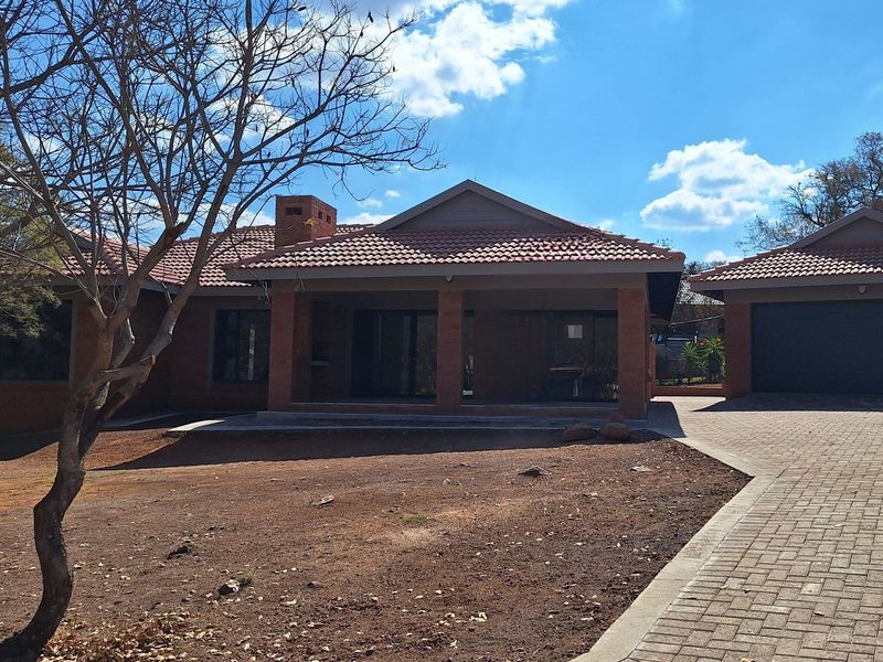 A single-story brick house featuring a tiled roof, covered patio, and an attached garage with a paved driveway.