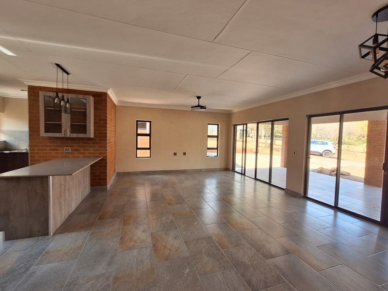 Spacious open-plan living area featuring tiled flooring, exposed brick accents, a breakfast bar, and large sliding glass doors leading to the outdoor patio.