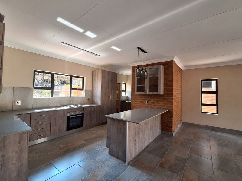 Modern kitchen featuring wood-look cabinetry, stone countertops, a central island, built-in oven and hob, and a distinctive exposed brick feature wall.