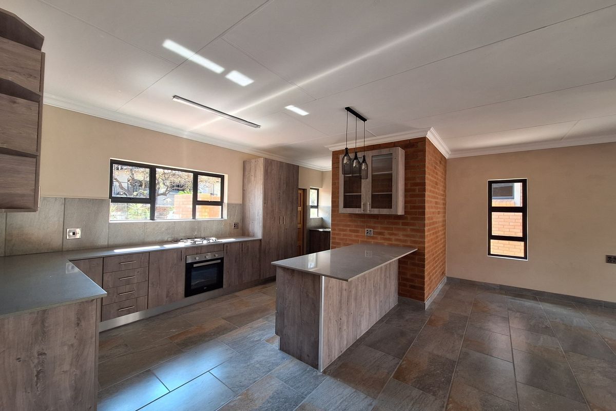 Modern kitchen featuring wood-look cabinetry, stone countertops, a central island, built-in oven and hob, and a distinctive exposed brick feature wall.