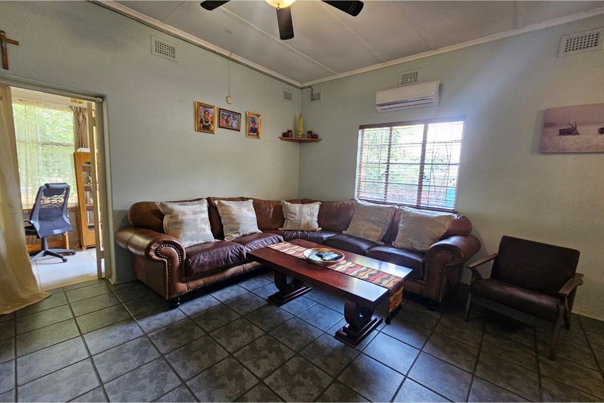 A comfortable living room featuring tiled flooring, a ceiling fan, and a wall-mounted air conditioning unit, with natural light entering through the window.
