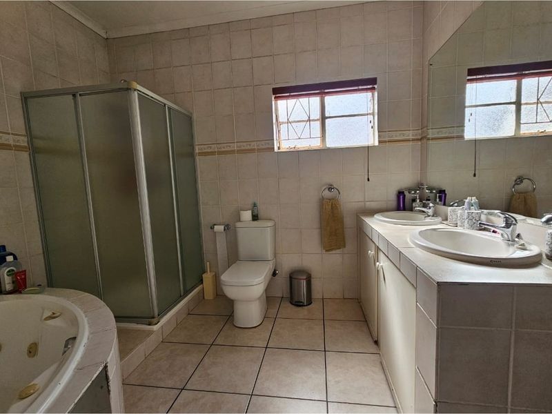 A functional bathroom featuring a corner spa bath, separate shower enclosure, dual vanity basins, and tiled finishes throughout.