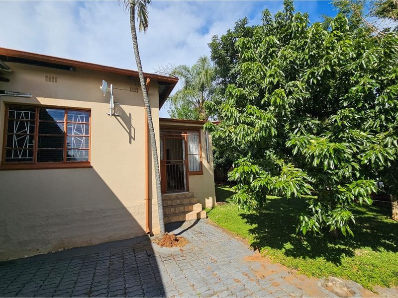 Rear view of the property featuring a paved walkway, established garden, and access to the home via a security gate.