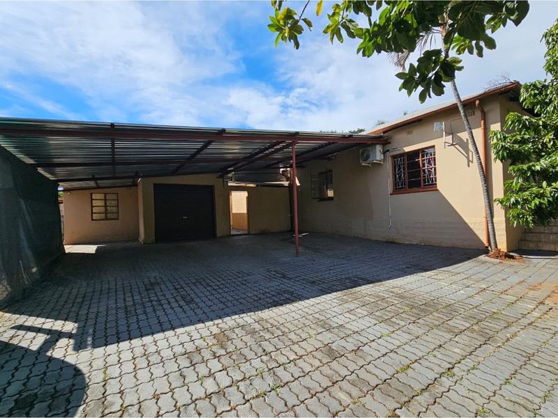 A paved driveway area featuring a large covered carport structure, providing ample off-street parking and access to the property entrance.