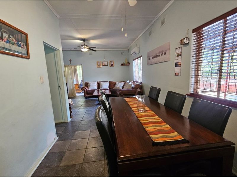 Open plan dining and living area featuring tiled flooring, ceiling fans, and large windows with wooden blinds.