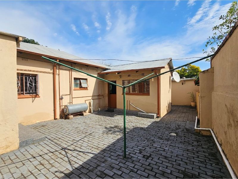 A rear exterior view of the property featuring paved courtyard area, metal security bars on windows, and a fixed rotary clothesline.