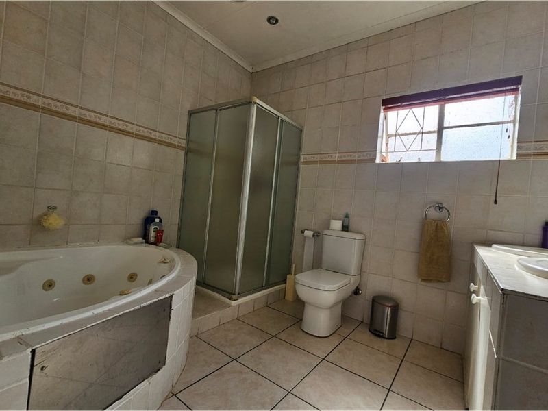A functional bathroom featuring a corner jetted bathtub, a separate glass-enclosed shower, a toilet, and a vanity basin with tiled walls and flooring.
