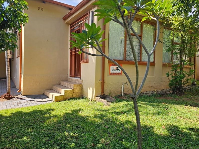 Exterior view of the side entrance featuring a paved walkway, small concrete steps, and established garden area with security signage.