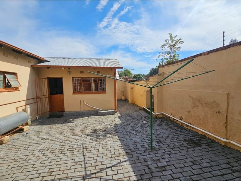 A paved rear courtyard area featuring a brick boundary wall, exterior access door, and an external geyser unit.