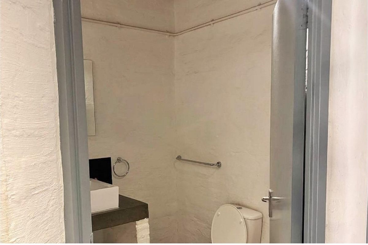 A compact bathroom featuring a concrete vanity with a vessel sink, a standard toilet, and exposed surface wiring on the walls.