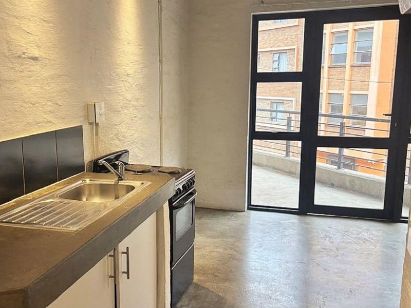 Compact kitchen area featuring a concrete countertop, stainless steel sink, and freestanding stove, with direct access to an outdoor balcony through a glass door.