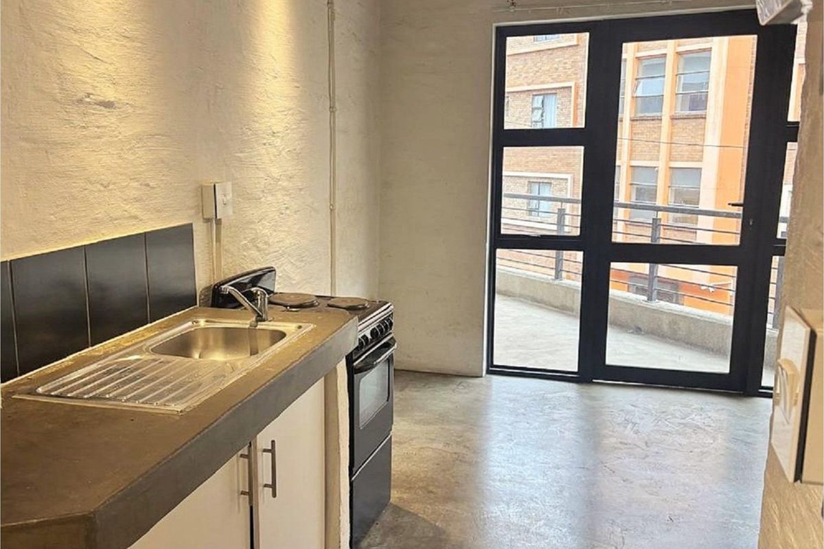 Compact kitchen area featuring a concrete countertop, stainless steel sink, and freestanding stove, with direct access to an outdoor balcony through a glass door.