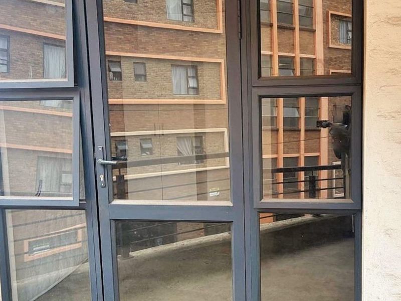 A view of an apartment balcony featuring dark aluminium framed glass doors and windows overlooking a neighbouring building.