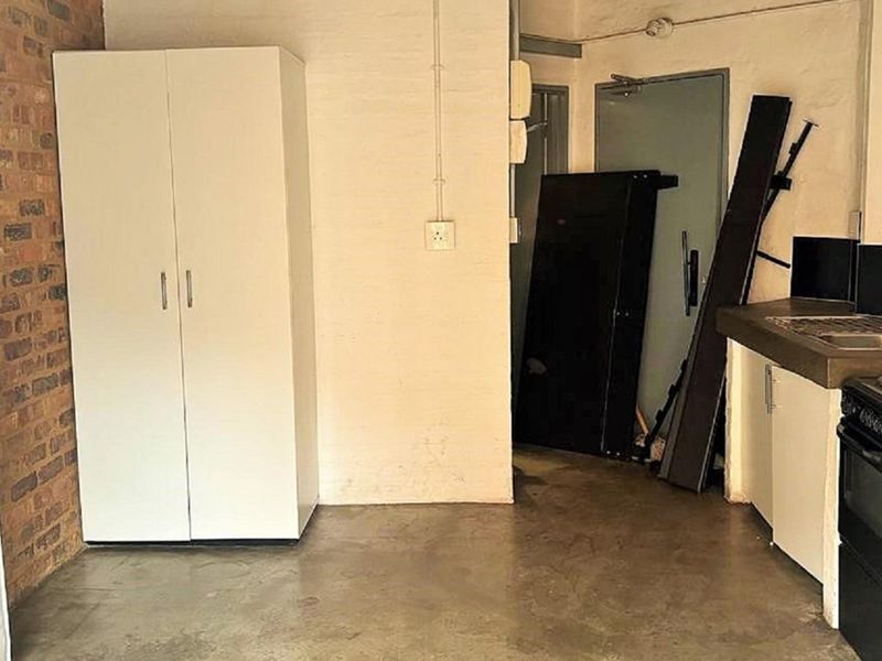 A functional kitchen area featuring exposed brickwork, concrete flooring, and basic cabinetry with a built-in sink and stove.