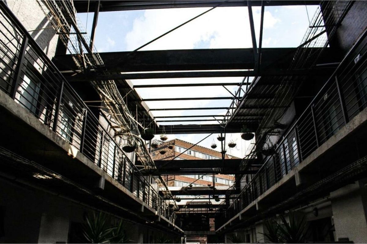 An industrial-style open-air atrium featuring exposed steel structural beams, concrete walkways, and metal railings, providing a unique architectural aesthetic for the apartment complex.