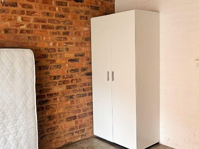 Bedroom featuring an exposed brick feature wall, concrete flooring, and a built-in white wardrobe.