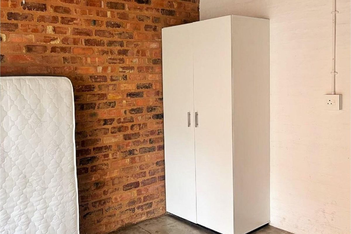 Bedroom featuring an exposed brick feature wall, concrete flooring, and a built-in white wardrobe.