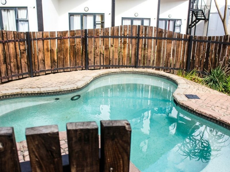 A private swimming pool area featuring stone paving and a wooden perimeter fence, set against the exterior facade of the apartment building.