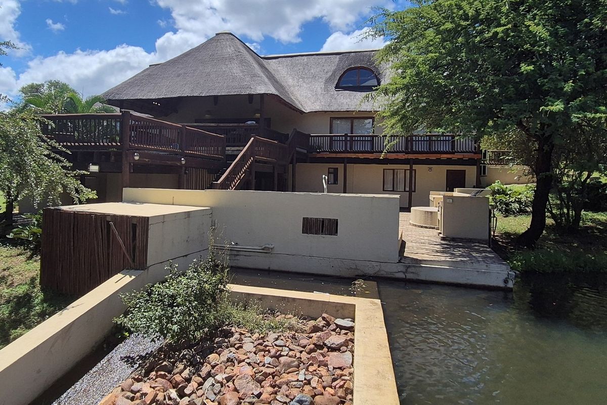 Rear view of a multi-level thatched roof house featuring extensive timber decking, a private patio area, and a landscaped water feature.