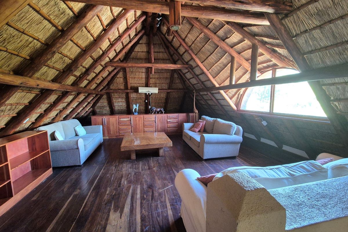 Spacious attic living area featuring a high vaulted thatched roof, exposed timber beams, dark wood flooring, and built-in cabinetry.