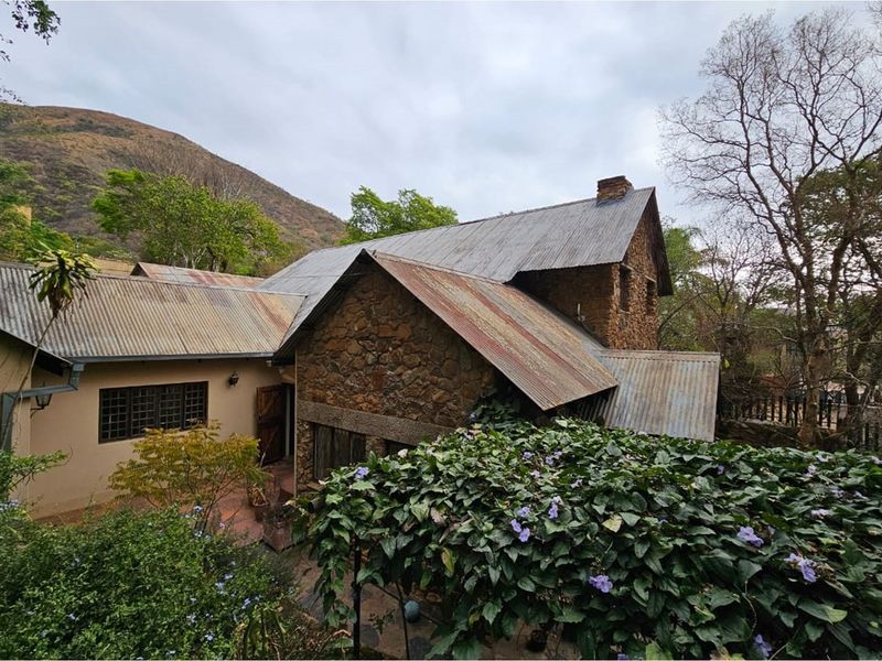 Elevated view of a rustic stone cottage featuring traditional corrugated metal roofing and established garden surroundings in a scenic mountain setting.