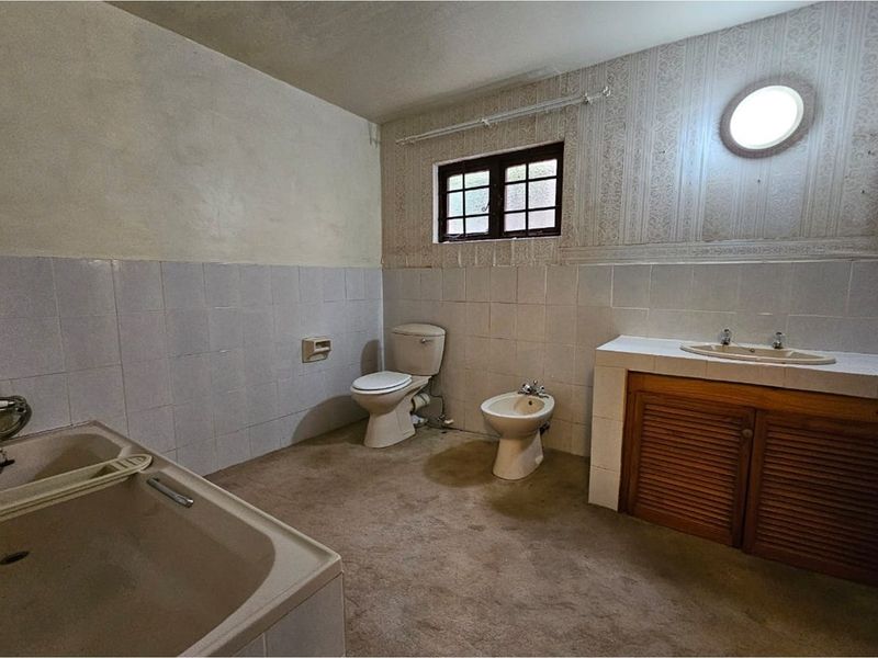 A dated bathroom featuring a built-in bathtub, toilet, bidet, and vanity cabinet with a tiled countertop, requiring modernization and renovation.
